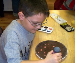 Close Up of a Boy Dotting with Puffy Paint on a ceramic plate at a claytopia class